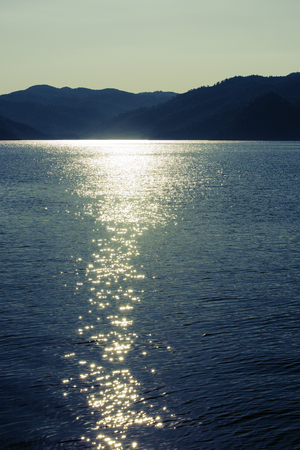 Twilight seascape. Mountains and sun glint in the waterの写真素材