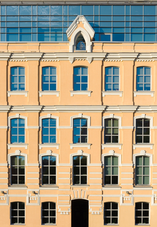The facade of the yellow building with glass Windows and an attic floor. Architectural details of the urban landscapeの写真素材