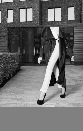 A young woman in a beautiful black coat and white trousers walking down the street. Black and white fashion portraitの写真素材