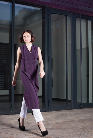 Young woman in beautiful purple dress walking down the street. Outdoor fashion portraitの写真素材