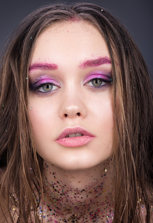 Closeup beauty portrait of beautiful girl teenager. Bright makeup with glitter. Sensual look. Neutral dark gray backgroundの写真素材