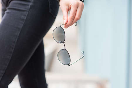 A stylish accessory. Close-up of sunglasses in a woman's hand. Outdoor portraitの写真素材