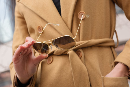 A woman in a coat holds sunglasses. Close-up outdoorsの写真素材