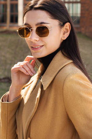 Portrait of a stylish young woman in a coat and sunglasses outdoorsの写真素材