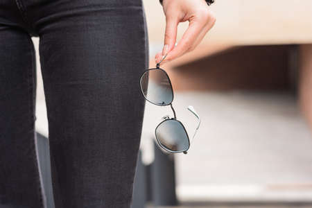 A stylish accessory. Close-up of sunglasses in a woman's hand. Outdoor portrait.の写真素材
