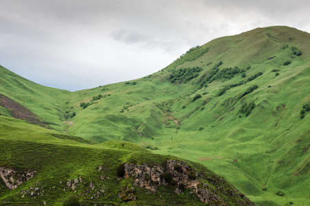 Rocky mountains and hills of Elbrus with low gray sky. Green lanscapeの写真素材