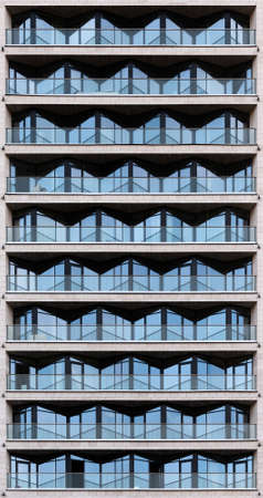 The facade of the city building faced with gray stone. Triangle prismatic windows reflect the blue sky.の写真素材