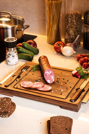 Ingredients for light snack. Smoked sausage on a wooden board with bread and fresh vegetables.の写真素材