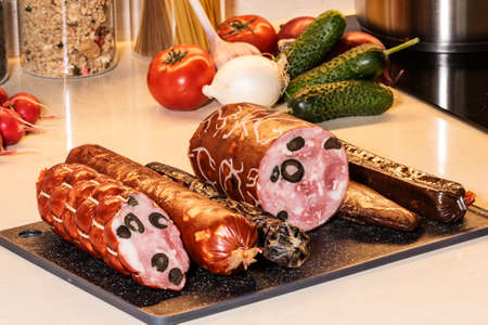 Italian sausage platter on the kitchen board. Cured sausages with fresh vegetables at the background.の写真素材
