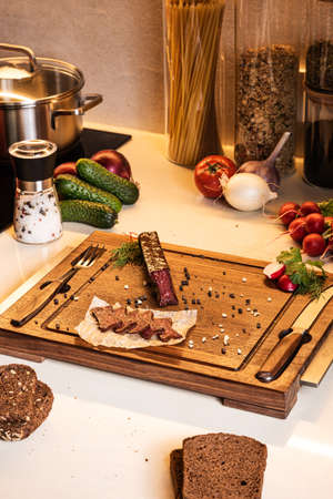 Ingredients for light snack. Cured sausage served on a wooden board with pepper, salt and bread.の写真素材