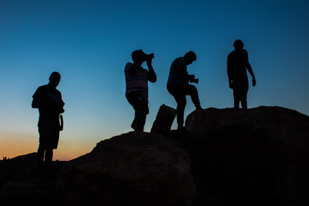 silhouette of Group of male photographers standing or taking photograph on top the mountain in evening sunset with blue sky on the backgroundの写真素材