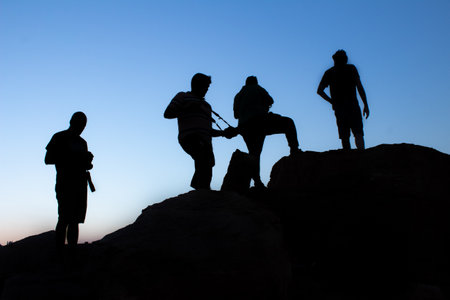 silhouette of Group of male photographers standing or taking photograph on top the mountain in evening sunset with blue sky on the backgroundの写真素材