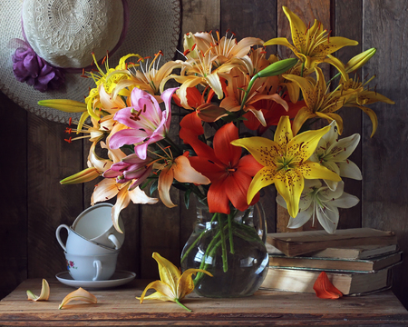 Still-life with a bouquet of lilies in a glass jar, summer hats, books and cups.の写真素材