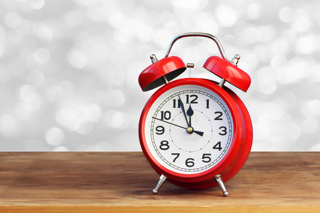 Red retro alarm clock at twelve o'clock on white bokeh abstract background. Midnight, midday. Minutes about New year. The concept of the celebration.の写真素材