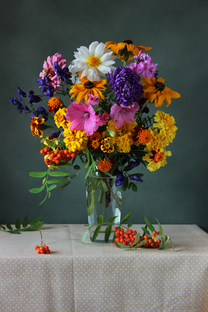 Beautiful autumn bouquet of garden flowers and branches of mountain ash in a vase on the table with a tablecloth in polka dots. Still life.の写真素材
