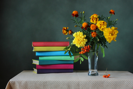Back to school. The teacher's day. Bouquet of autumn flowers and a stack of books in the colored cover on the table with a tablecloth in polka dots. Still life.の写真素材