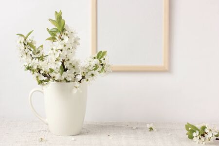 blooming plum branches with white flowers in a Cup and an empty wooden frame with space to copy....