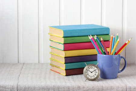 stack of books, colored pencils, and an alarm clock on the table. back to school, knowledge day....