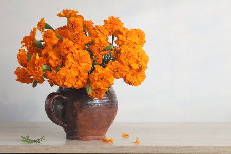 Bright orange marigold flowers are arranged in a clay pot, placed on a light wooden table. The floral display adds warmth and color to a tranquil indoor setting, inviting a sense of calm.の写真素材