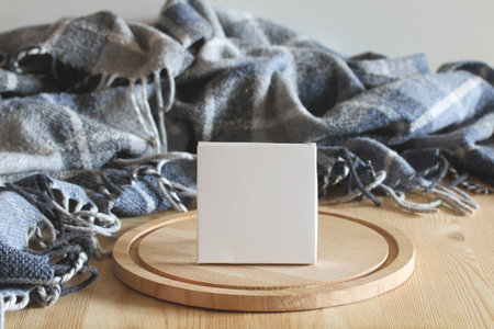 Small white cardboard box placed on a wooden board with a cozy blanket, perfect for showcasing product packagingの写真素材