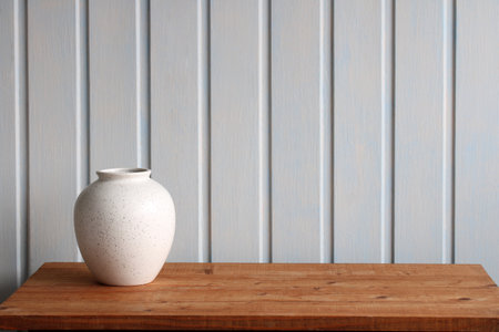 Minimalist still life featuring a white speckled ceramic vase on a wooden table against a light blue background, creating a clean and modern aestheticの写真素材