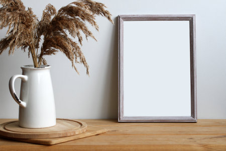 Home decor with blank frame mockup, dried flowers in jug and wooden cutting boards on a tableの写真素材