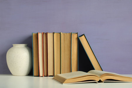 Composition of old books and a vase on a white table with purple background, perfect for book lovers and knowledge seekersの写真素材