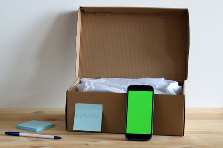 Cardboard box with return label and smartphone with green screen showing how to return online orders