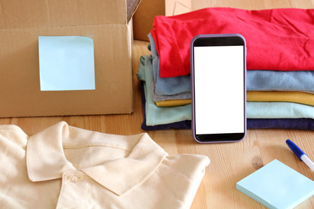 Online seller preparing clothes for shipping with mobile phone and cardboard box