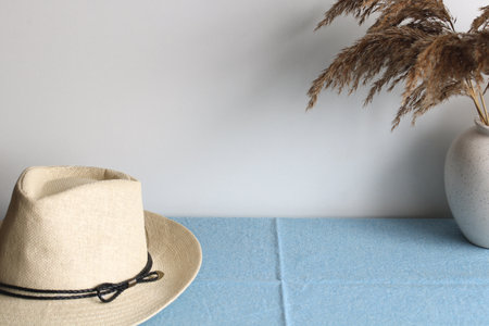 Minimalist still life composition featuring a straw hat, pampas grass, and a light blue tablecloth, creating a serene and stylish scene. boho style, an empty space for your textの写真素材