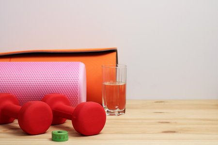 Fitness accessories like foam roller, dumbbells, yoga mat and juice glass are laying on wooden surface, promoting healthy lifestyleの写真素材