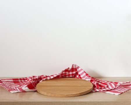 Round wooden cutting board and red and white checkered napkin on wooden table against white backgroundの写真素材