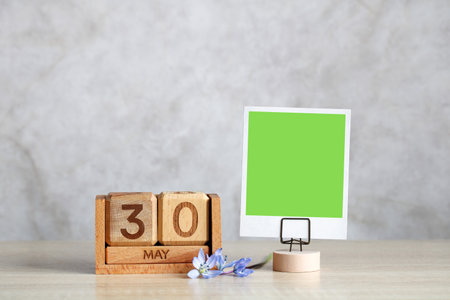 Wooden calendar showing may 30th with green screen photo frame and flowers on a tableの写真素材