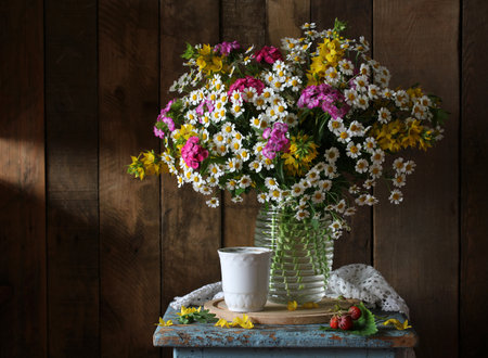 A lush bouquet of summer flowers in a transparent vase is placed on an old blue stool. still life with cute daisies, yellow loosestrife and pink Turkish carnations.の写真素材