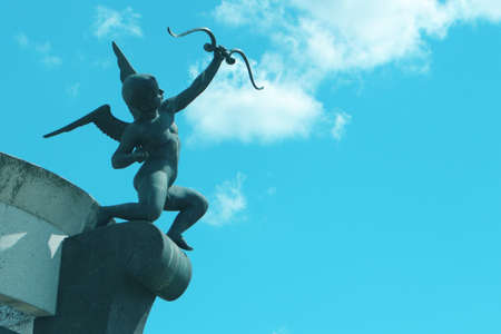 Cupid - angel with a bow against the blue sky. An old sculpture. Toned photo.