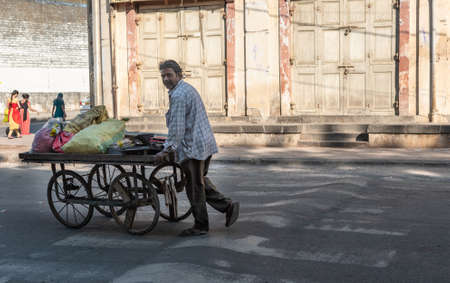 Junagadh, Gujarat, India - December 2018: A street vendor pushes his cart past the closed shutters of shops on the market streets of the city.のeditorial素材