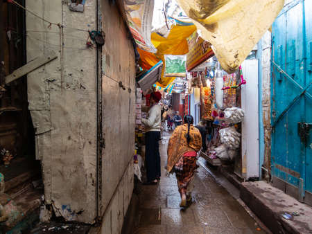 Varanasi, Uttar Pradesh, India - February 2015: A woman walking through a narrow alley lined with shops in the old city.のeditorial素材