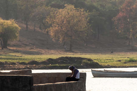 Nagpur, Maharahstra, India - March 2019: A young Indian girl wearing a veil sitting alone by beautiful setting of the Futala lake in the city.のeditorial素材