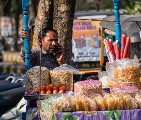 Nagpur, Maharahstra, India - March 2019: An Indian street vendor selling snacks by the roadside and talking on the phone.のeditorial素材