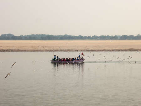 Varanasi, Uttar Pradesh, India - February 2015: Pilgrims take  a ride on an old wooden boat on the river Ganga with a large flock birds flying around.のeditorial素材