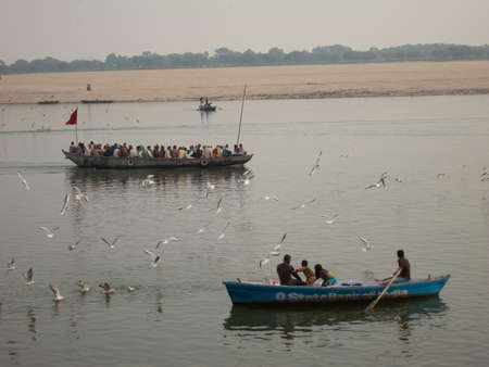 Varanasi, Uttar Pradesh, India - February 2015: Pilgrims take a ride on wooden boats on the river Ganga with birds flying around.のeditorial素材