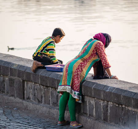 Nagpur, Maharahstra, India - March 2019: An Indian woman leaning over a stone wall to look at a lake.のeditorial素材