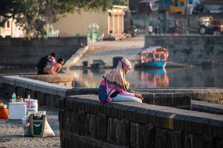 Nagpur, Maharahstra, India - March 2019: A young Indian girl wearing a veil sitting alone on a lakeside wall.のeditorial素材