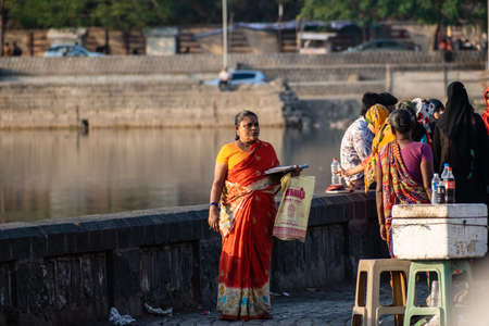 Nagpur, Maharahstra, India - March 2019: An Indian woman wearing a red sari standing by the lakeside...