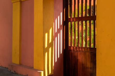 Light and shadow abstract with sunlight hitting the colorful walls outside a wooden door in the old city of Pondicherry.のeditorial素材