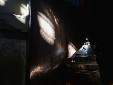 Trichy, Tamil Nadu, India - February 2020: Sunlight hitting the triangular metal roof of a shrine inside a dark hall at a Hindu temple.のeditorial素材