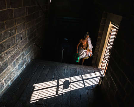 Trichy, Tamil Nadu, India - February 2020: A Hindu priest wearing a white dhoti in a dark passage inside the ancient Rockfort temple.のeditorial素材