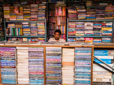 Trichy, Tamil Nadu, India - February 2020: A book seller sitting in a shop with stacks of academic books on the shelves.のeditorial素材