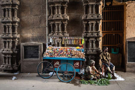 Trichy, Tamil Nadu, India - February 2020: Indian steet vendors selling jewellery and green leaves beside the ancient stonework on the gateway to the Hindu temple in Srirangam.のeditorial素材