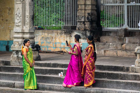 Mayiladuthurai, Tamil Nadu, India - February 2020: Indian women dressed in colourful saris smiling and laughing cheerfully while taking pictures with their mobile phones inside an ancient temple.のeditorial素材